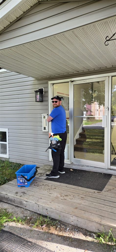 Window cleaner in a blue shirt with a tool belt beside a glass commercial entrance