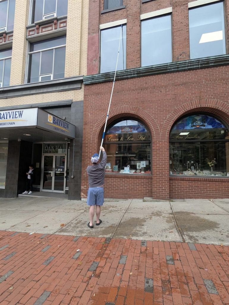 Cleaning upper windows of an Uptown Saint John building with a telescopic pole
