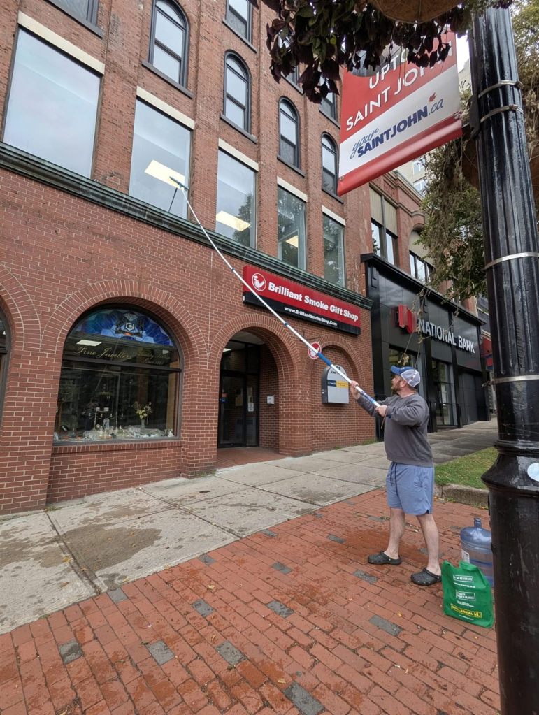 Fundy Blue cleaning second-floor windows of an Uptown Saint John brick storefront with a telescopic pole